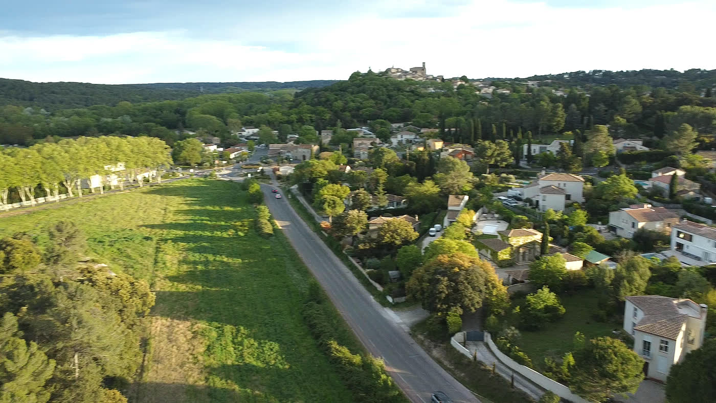 Vue aérienne d’un coteau résidentiel au soleil couchant, maisons, prairie et village perché à l’horizon